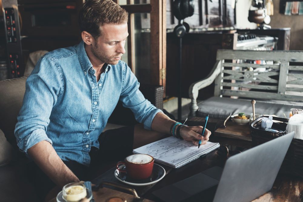 Man writing and looking at laptop